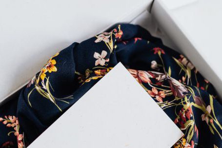 Luxury E-commerce - From above of stylish black silk floral pattern cloth with white visit card mockup placed in white carton box after receiving postal delivery of online order