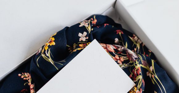 Luxury E-commerce - From above of stylish black silk floral pattern cloth with white visit card mockup placed in white carton box after receiving postal delivery of online order